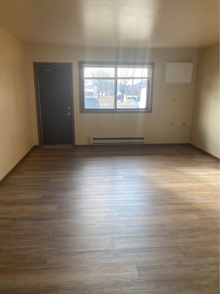 Living room with wood-look flooring, a wide window and a wall air conditioner